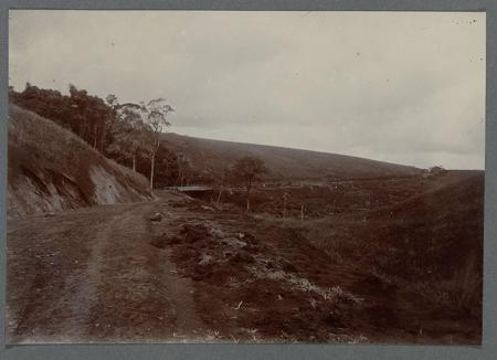Construction of the road with a bridge along a slope. Tipped-in photo in an album with 87 photos about the construction of the Gajoweg in North Sumatra between Bireuen and Takinguen between 1903-1914.