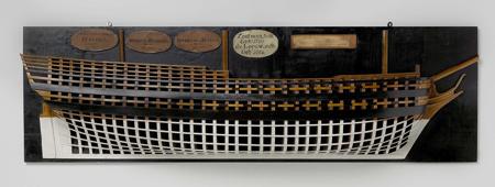 Polychrome mold model (starboard) of a three-master. The large number of frame templates is striking. No gun gates; barge deck and half deck can be distinguished by screams. Two knees at the bow. Twisted mirror, hollow wulf, no fence or side gallery; straight rudder with square rudder stock. The sheer rises at both ends, two mountain woods and one roe wood. Fairly flat underwater ship. Scale 1:55 (scale on model).